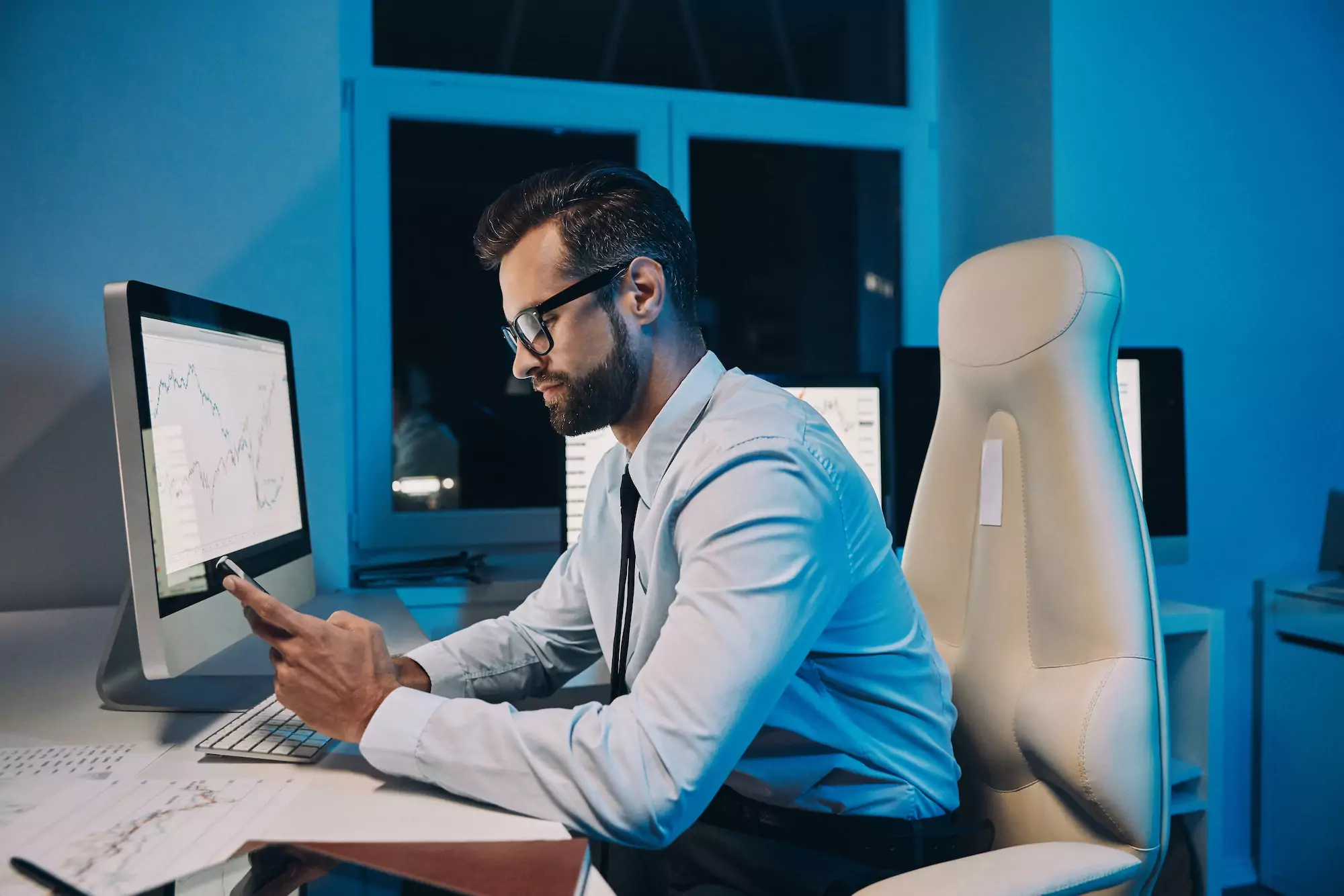 Handsome young man in shirt and tie using smart phone while staying late in the office