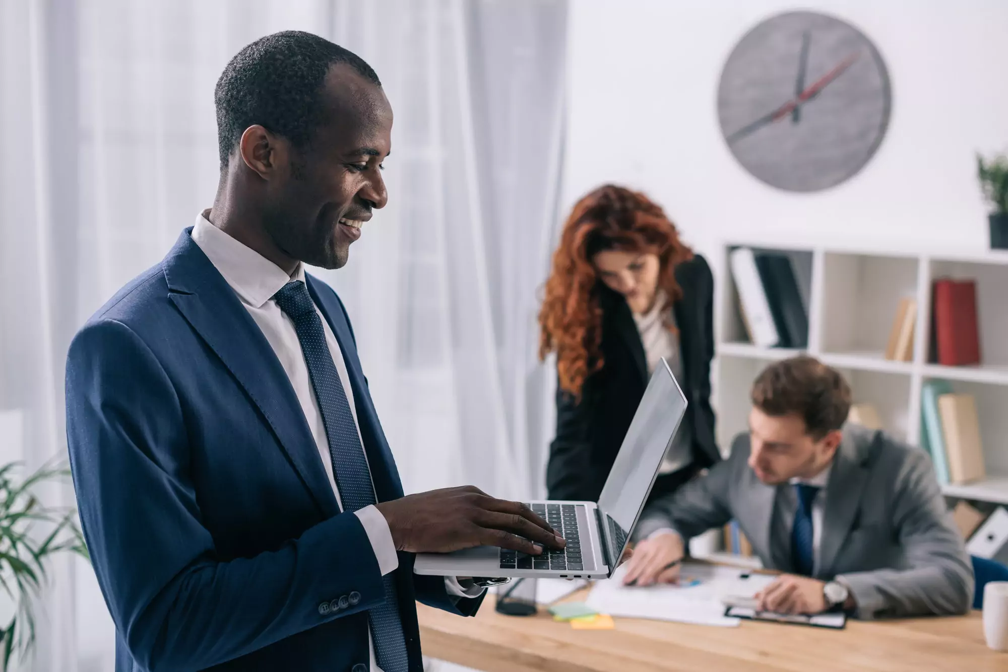 Smiling african businessman with laptop in hands and two business colleagues working at table