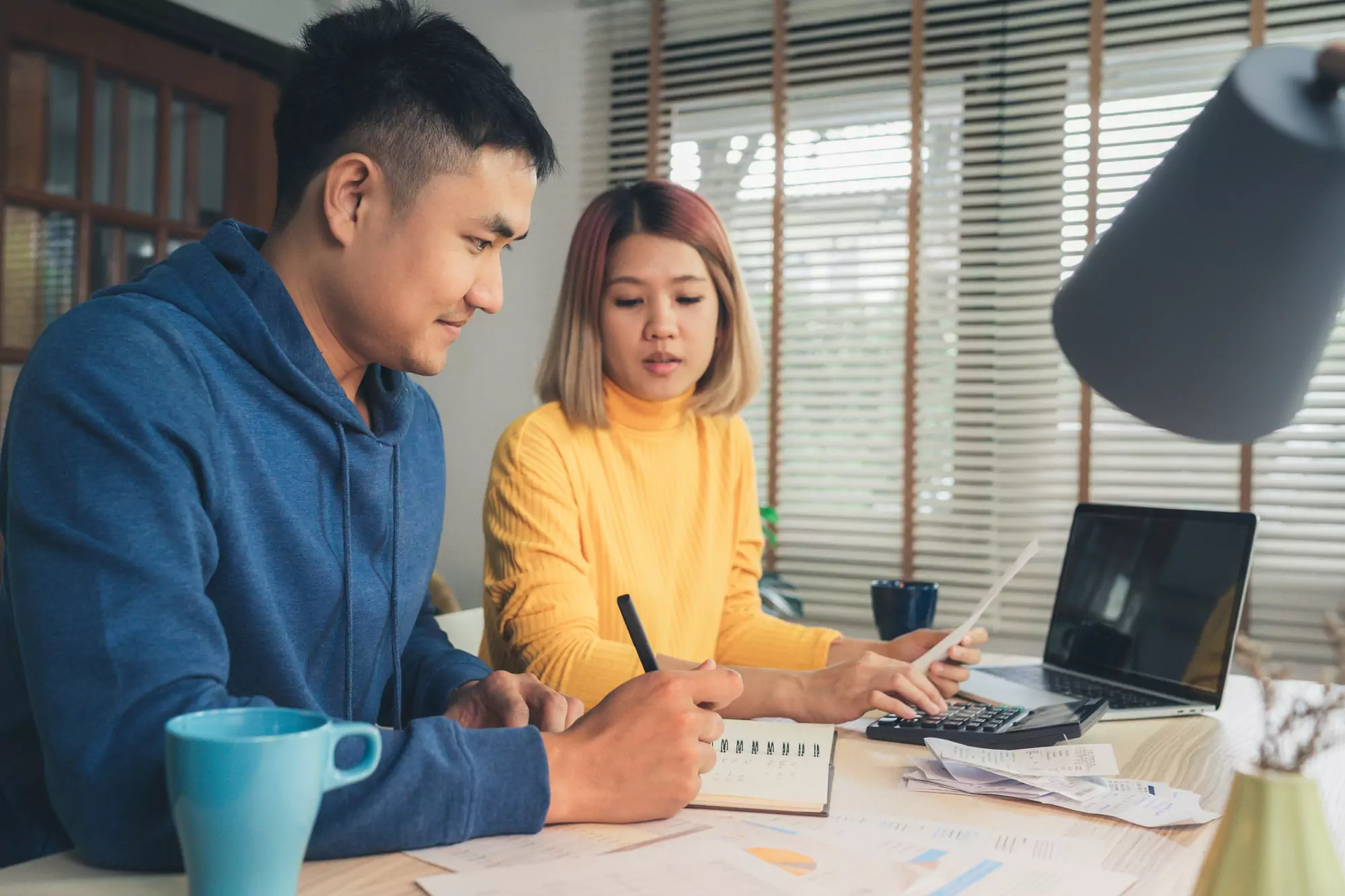 Young asian couple reviewing their bank accounts using laptop computer and calculator.